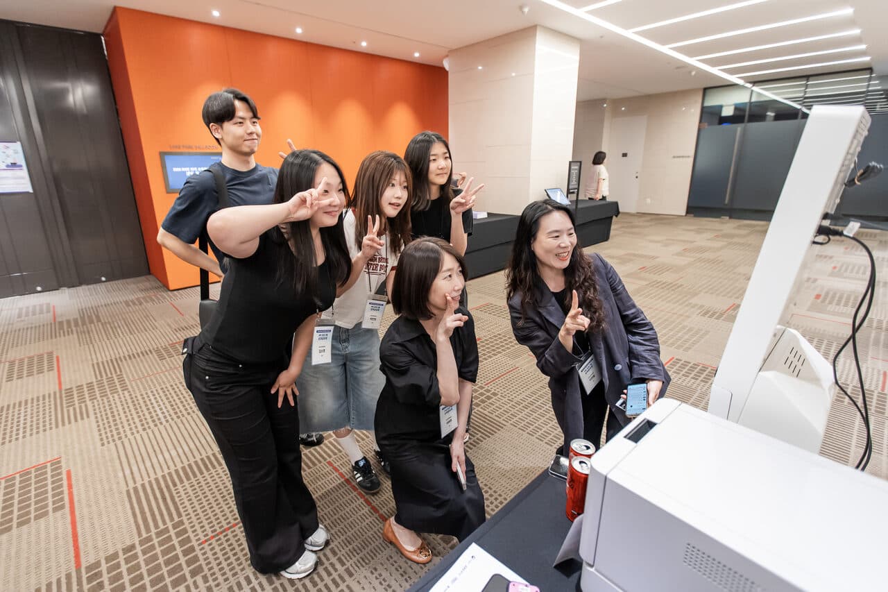 포토부스 카메라 앞에서 단체로 포즈를 잡은 참석자 다섯 명