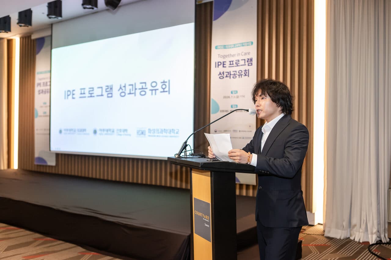 코트야드 바이 메리어트 수원 레이크파크볼룸에서 열린 IPE 프로그램 성과공유회 개회 — 스크린에 행사 타이틀이 표시되고 사회자가 포디움에서 진행 중